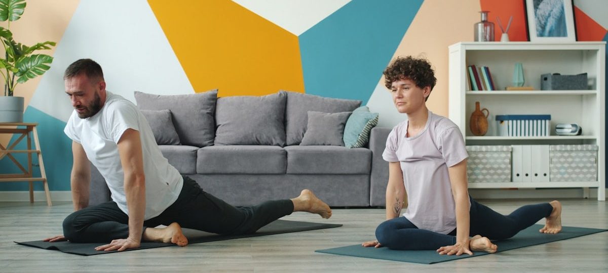 Young couple man and woman are doing yoga at home exercising together on mats practising asanas in apartment moving simultaneously. Youth and sports concept.