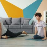 Young couple man and woman are doing yoga at home exercising together on mats practising asanas in apartment moving simultaneously. Youth and sports concept.